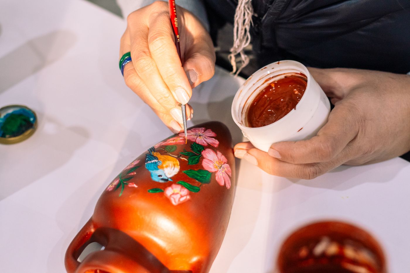 An artist hand-painting a bird onto a clay vase