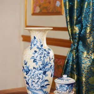Blue-and-white ceramic vase and cup with floral designs on an ornate table.