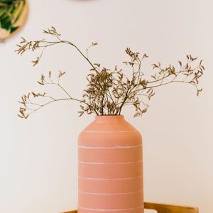Terracotta vase with dried flowers resting in a wooden tray.