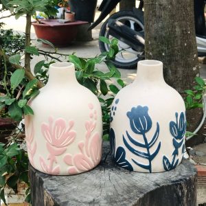 A pair of ceramic vases with painted floral patterns set on a tree stump.