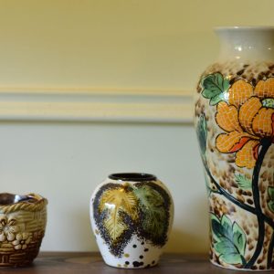 Three decorative ceramic vases with floral designs arranged on a wooden shelf.